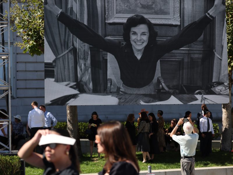 A large photo of Dianne Feinstein on a banner in front of a group of people.