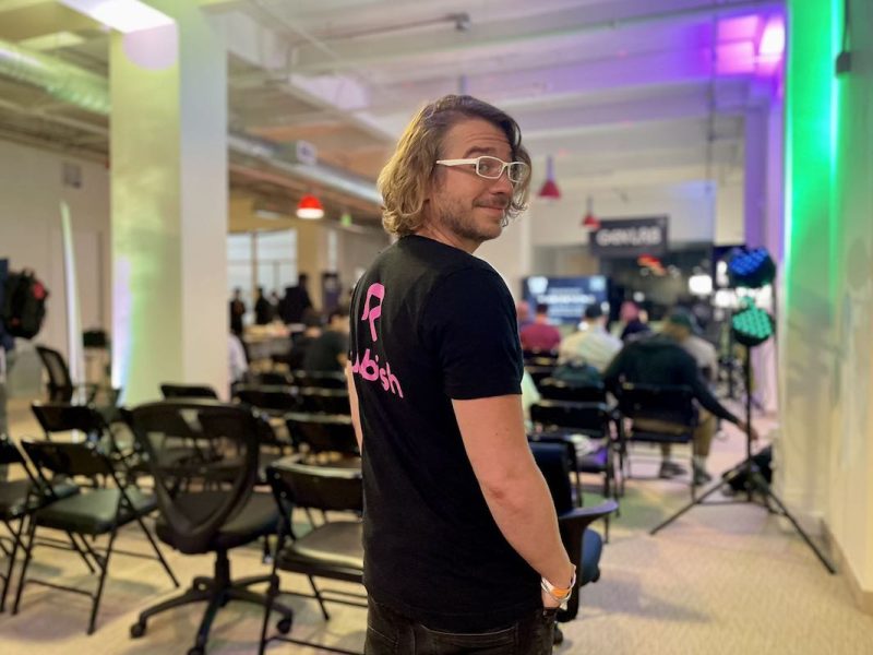 A man in a pink shirt is captured standing in an empty room.