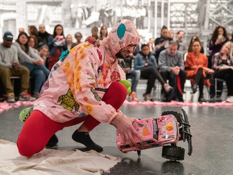 A man in a pink costume kneeling on the floor in front of a crowd.