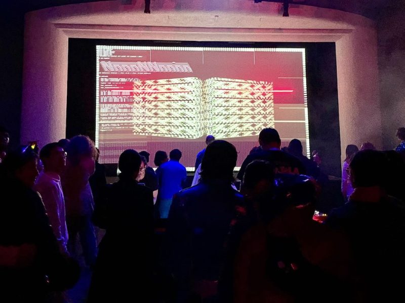An AV club algorave in front of a large screen.
