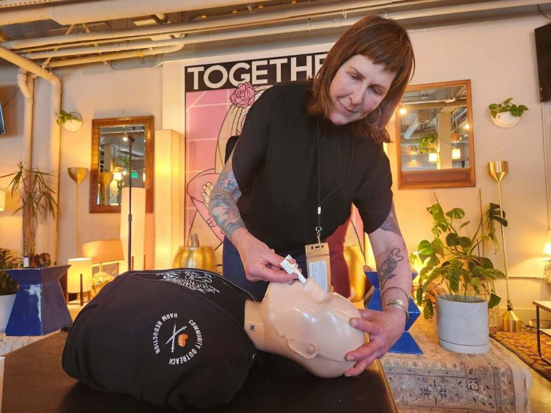 a woman demonstrating a Narcan nasal spray on a dummy