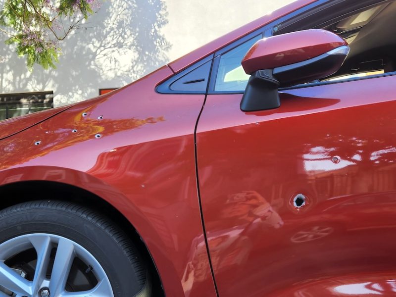 The front left of a red car with bullet holes in it