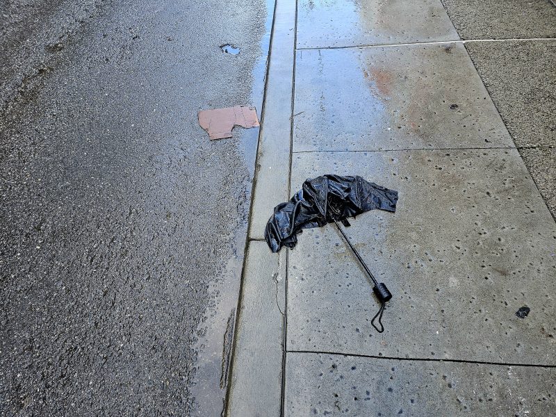 A black umbrella laying on the sidewalk.