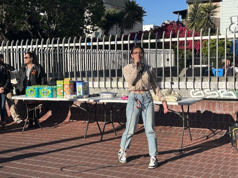 A young woman in glasses sings at a transit courtyard.