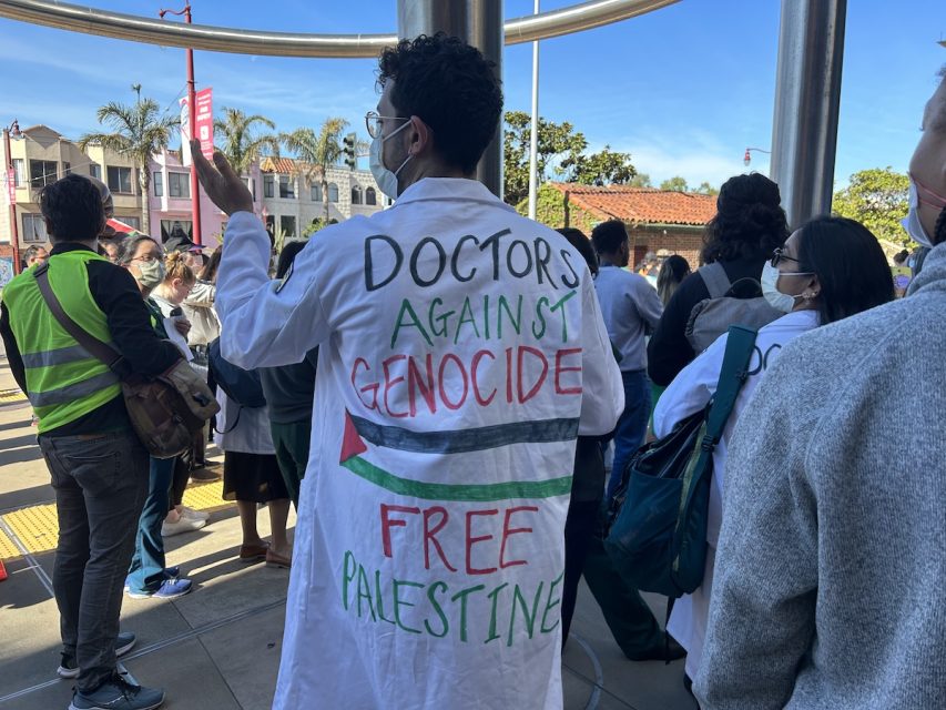 A group of people standing in front of a sign that says doctors against genocide.