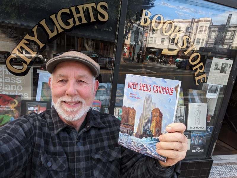 Chris Carlsson holding his new book When Shells Crumble, in front of San Francisco bookstore City Lights Books.