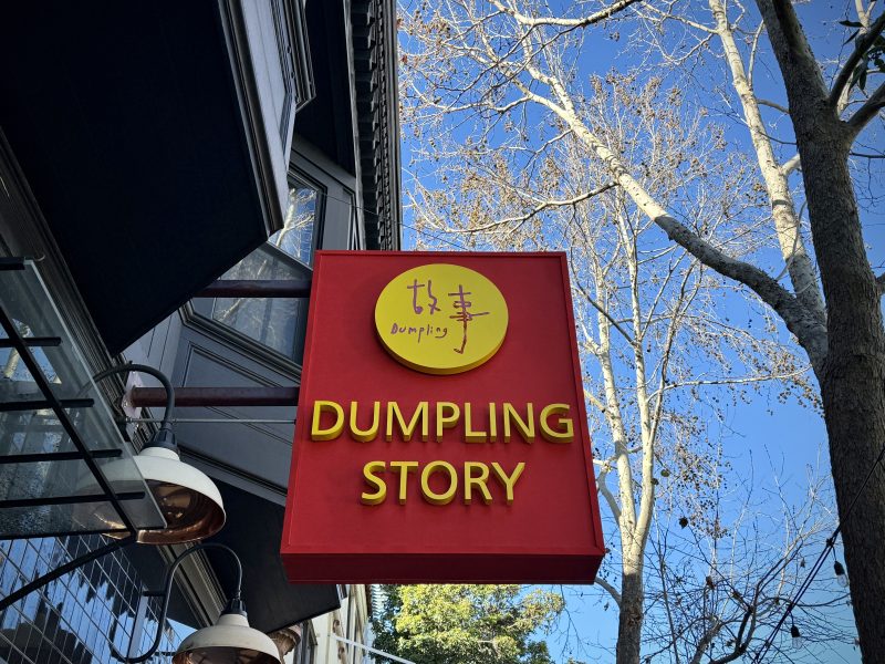 A sign that says dumpling story hangs from the side of a building.