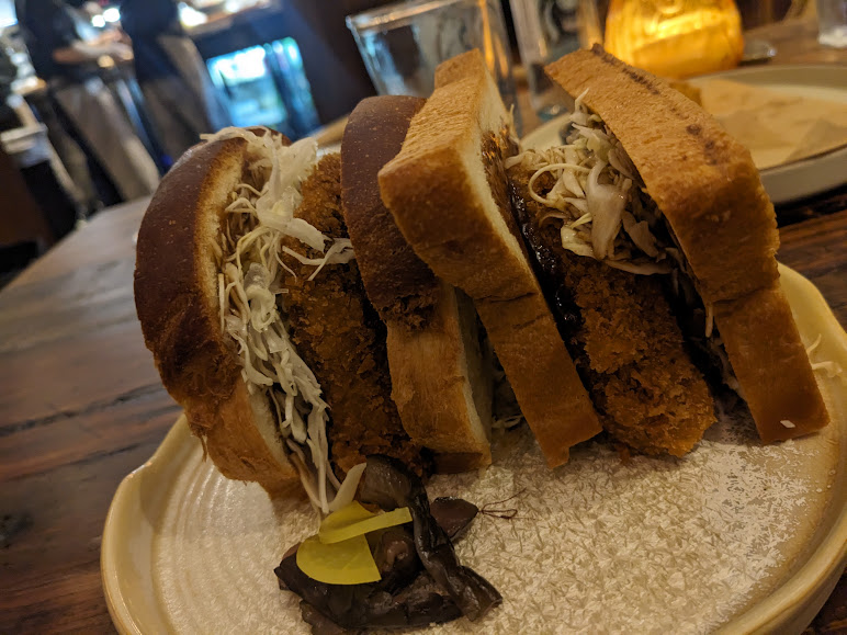 A sandwich is sitting on a plate in front of a bar.