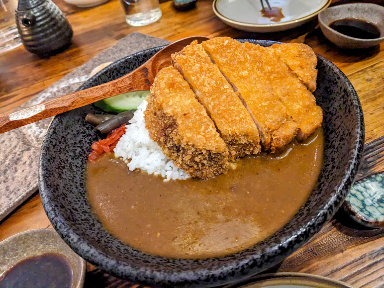 A bowl of curry with meat and rice on a wooden table.
