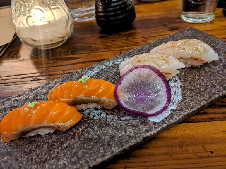 Three pieces of sushi are sitting on a stone plate.