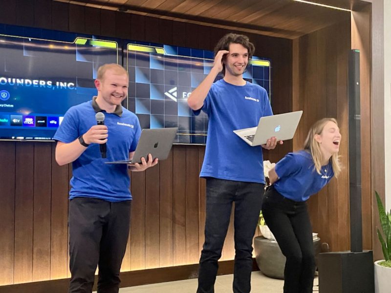 Three people standing in front of a screen with laptops.