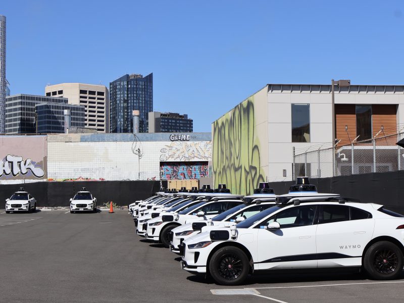 A group of Waymo cars parked in a parking lot.