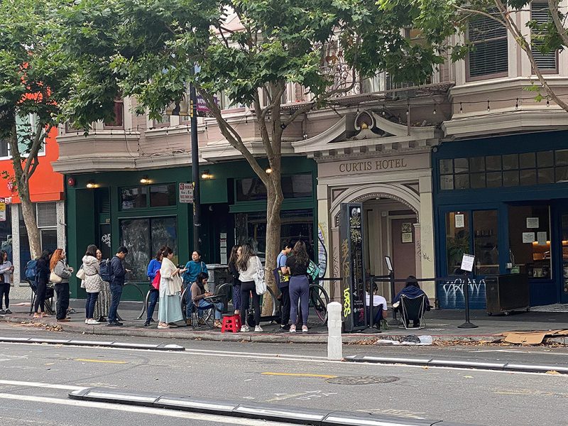 An urban street with line of patrons, some in chairs