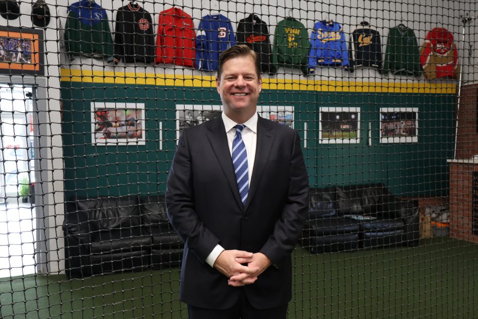 A man in a suit standing in front of a baseball netting.
