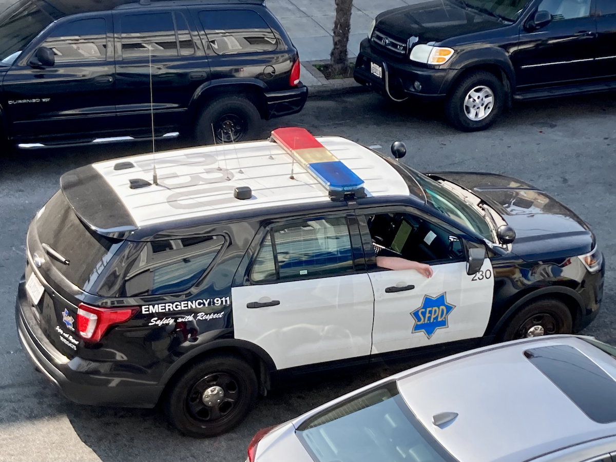 San Francisco police car driving on a street between parked cars