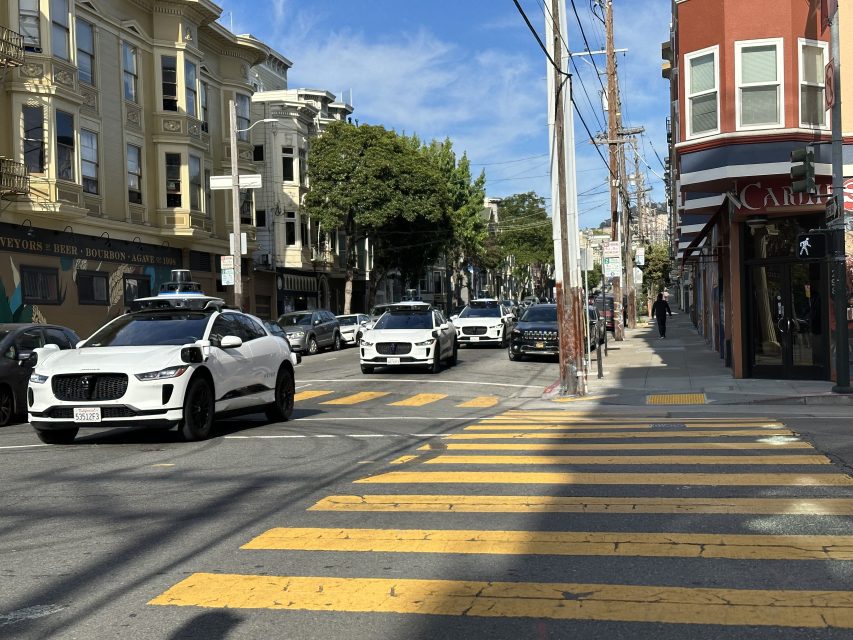 Three Waymo self-driving cars back to back, cruising down a street in the Mission