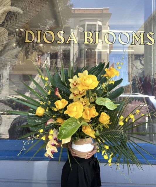 A woman holding a yellow bouquet in front of a store.