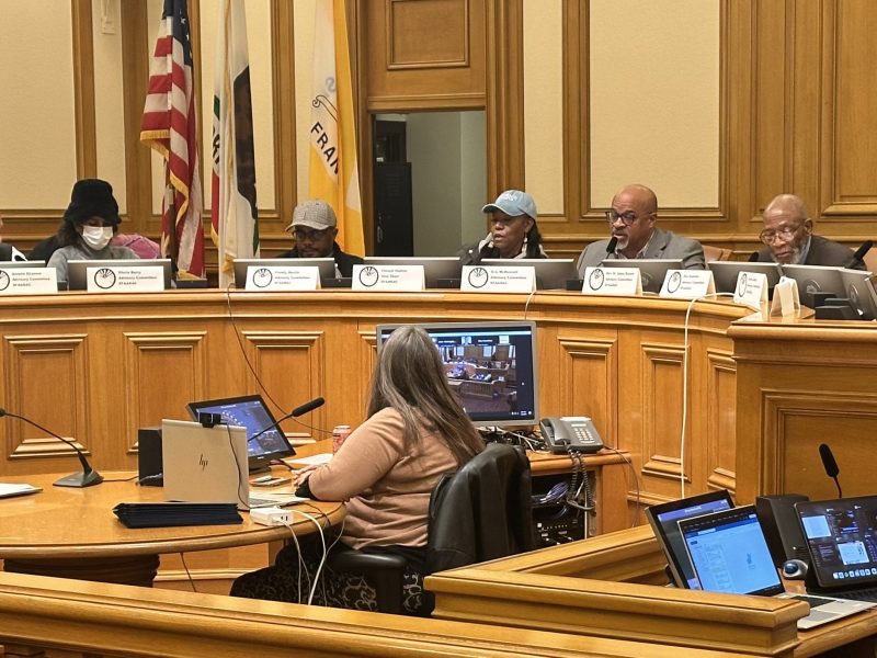 Members of San Francisco's reparations task force meeting on their final day, sitting in front of a dais.