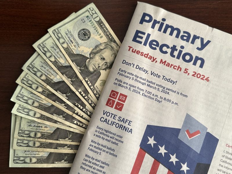 A March 5, 2024, voter information guide on top of a stack of $20 bills.