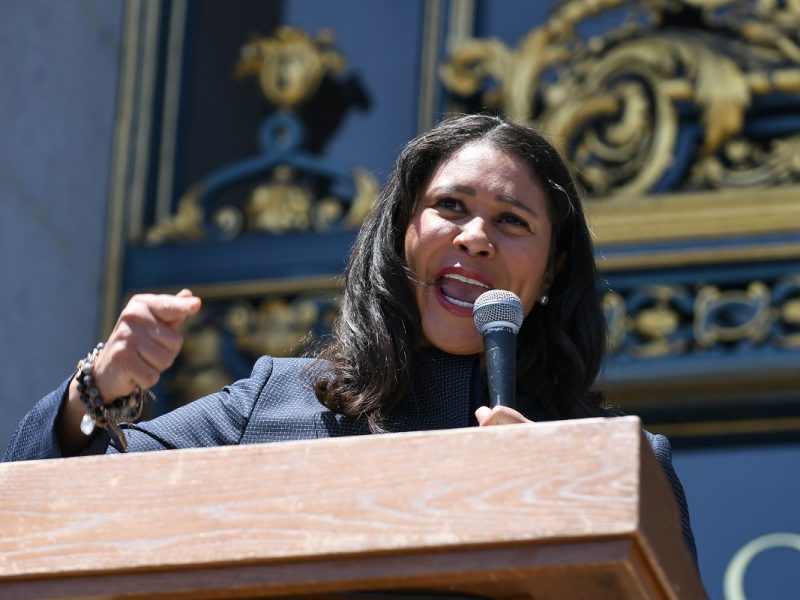 Mayor London Breed speaking into a microphone outside City Hall.