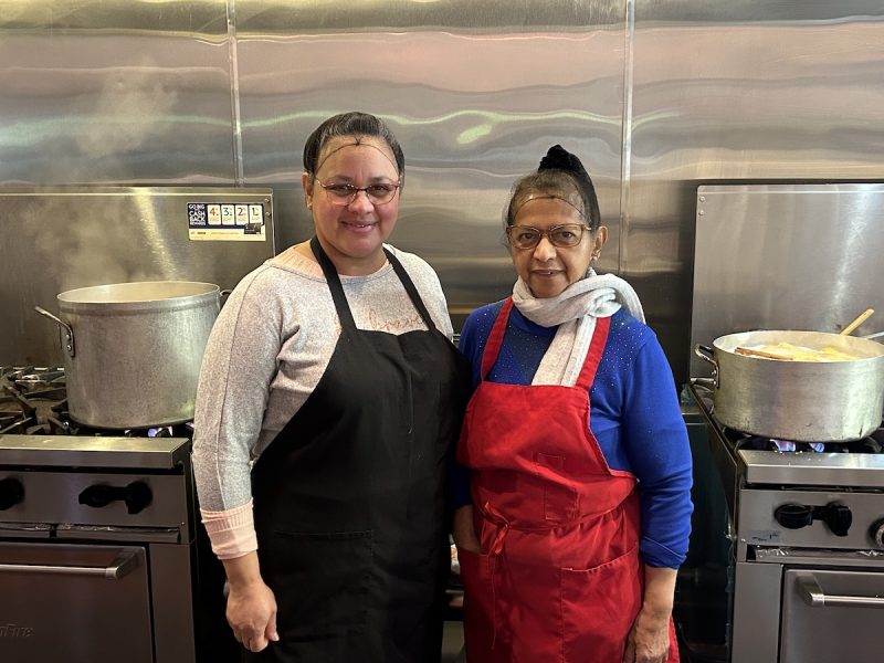 Two women in aprons standing in front of a kitchen.