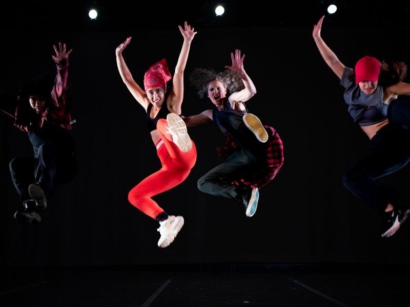 Four dancers jumping in the air on stage for a performance of Match Girrl