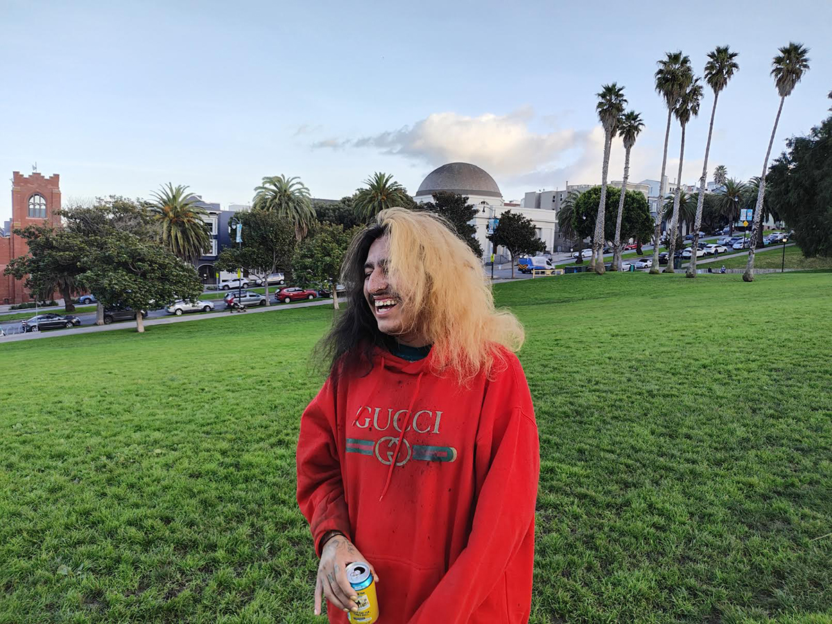 DJ NanosauR in a red hoodie standing in a park.