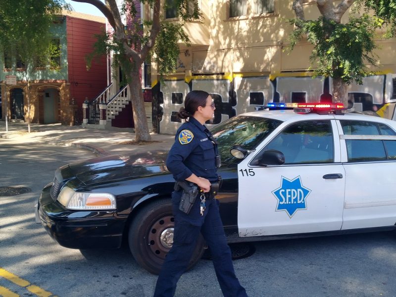 SFPD police officer walks past squad car.