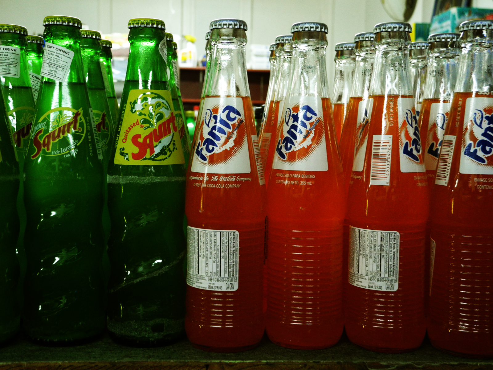 Bottles of soda are lined up on a shelf.