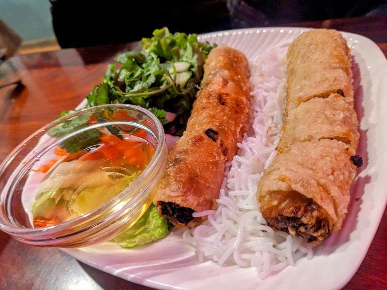 Vietnamese spring rolls on a plate with rice and a dipping sauce.