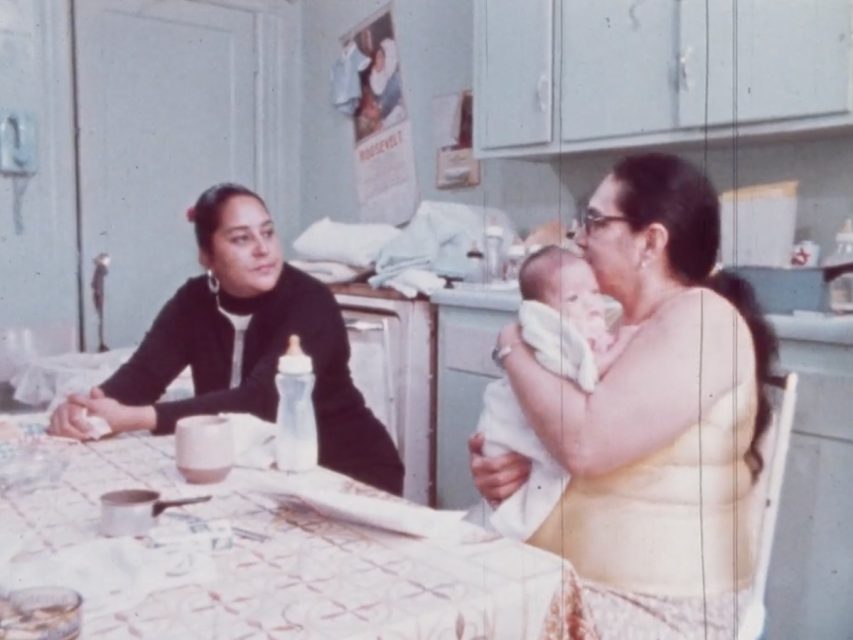 Two women sitting at a kitchen table. One of them is holding a baby.