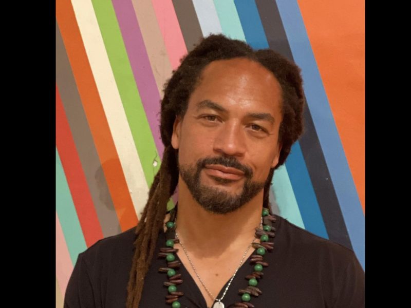 A man with dreadlocks standing in front of a colorful wall.