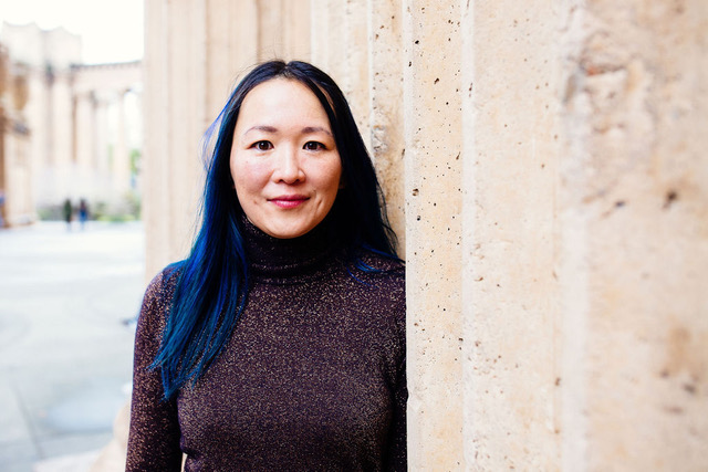 A woman with blue hair leaning against a wall.