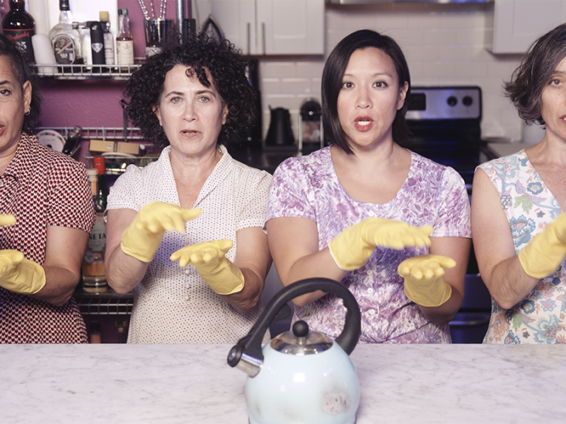 A group of women in yellow gloves holding a tea kettle.
