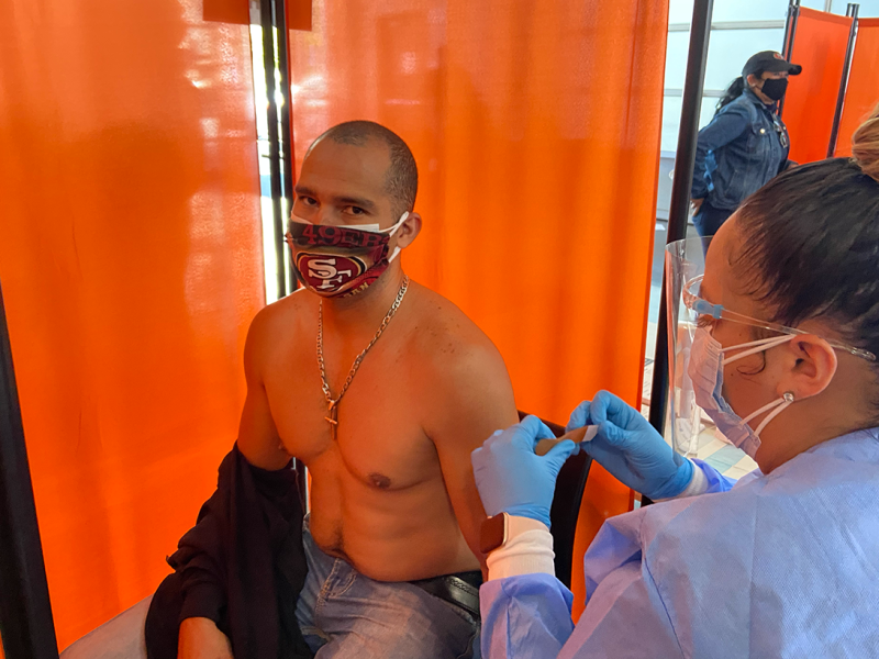 A nurse readies a shirtless man's arm for a Covid-19 vaccine.