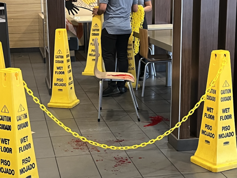 A pool of red liquid on a chair and on the floor at McDonald's, surrounded by Wet Floor cones.